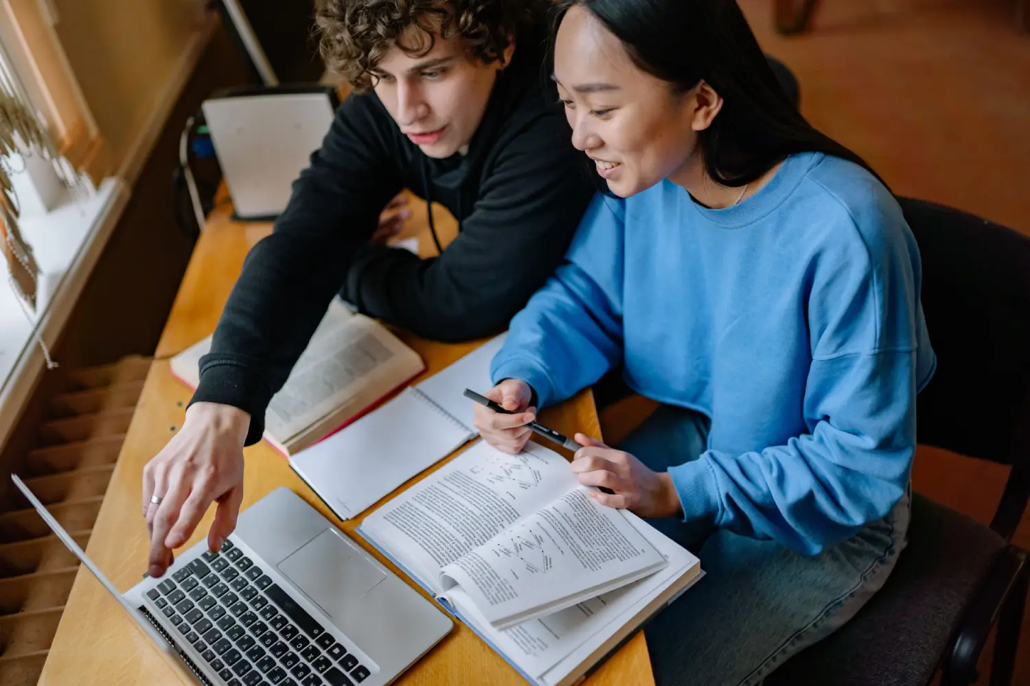 Two students studying together with a laptop and textbooks Yan Krukau 